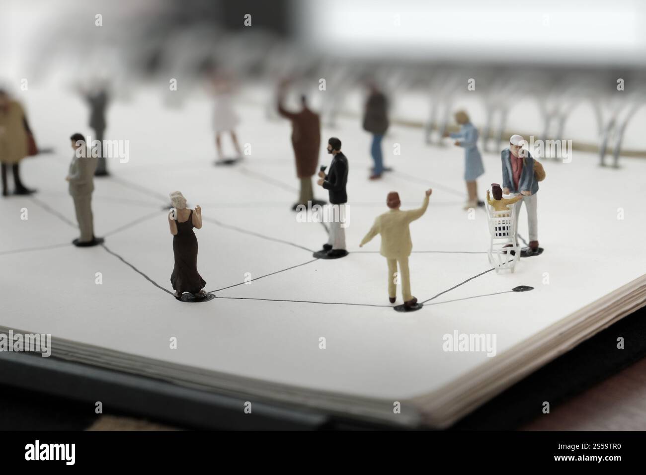 primo piano di persone in miniatura con un diagramma di social network su un notebook aperto su una scrivania in legno mentre i social media si avvicinano Foto Stock