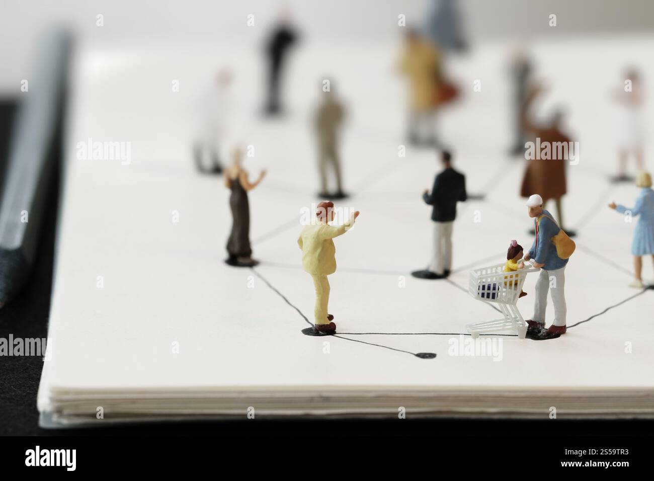 primo piano di persone in miniatura con un diagramma di social network su un notebook aperto su una scrivania in legno mentre i social media si avvicinano Foto Stock