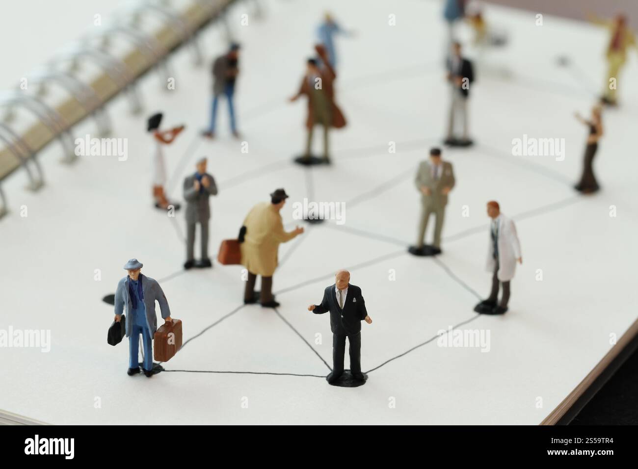primo piano di persone in miniatura con un diagramma di social network su un notebook aperto su una scrivania in legno mentre i social media si avvicinano Foto Stock