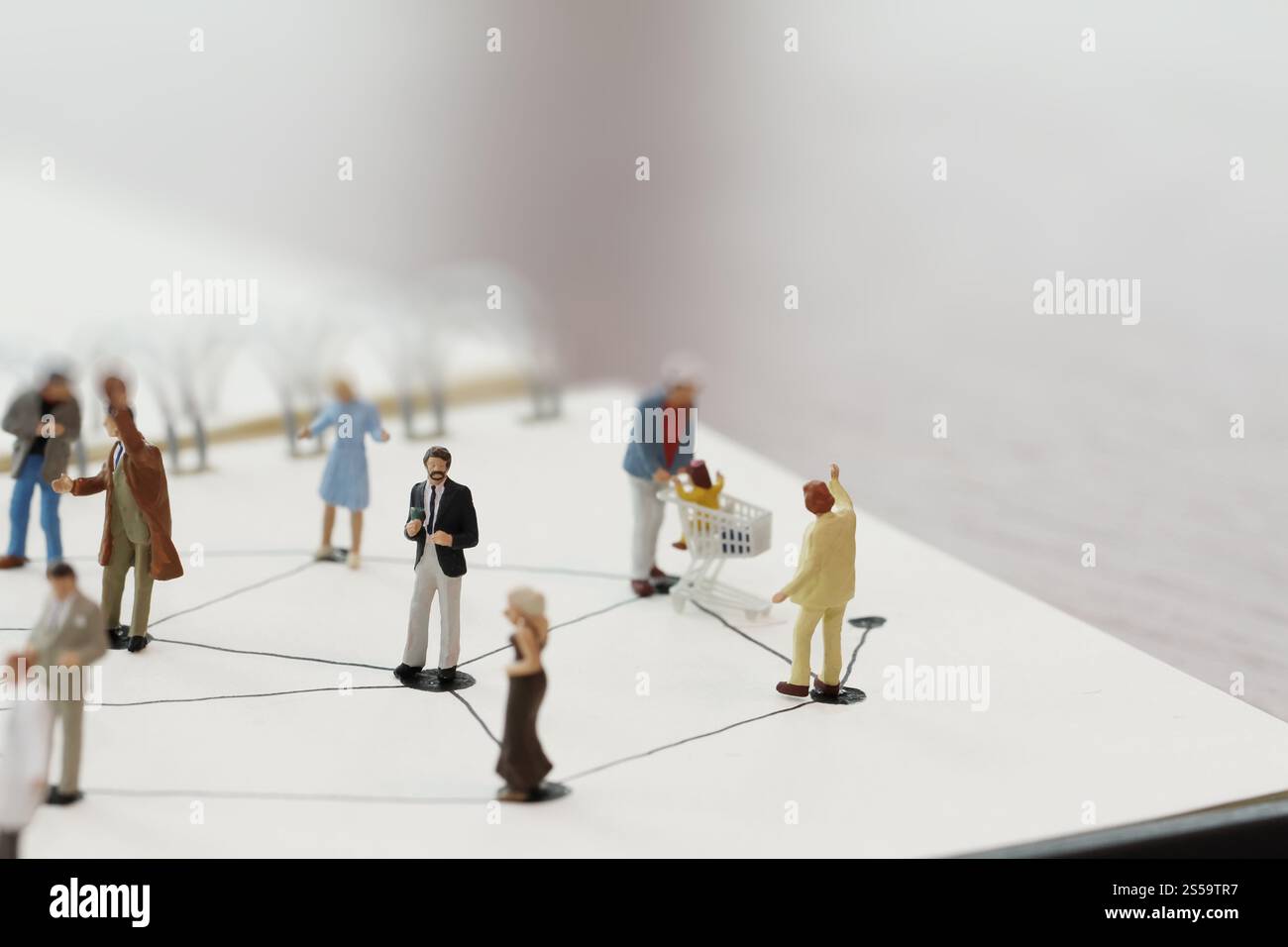primo piano di persone in miniatura con un diagramma di social network su un notebook aperto su una scrivania in legno mentre i social media si avvicinano Foto Stock