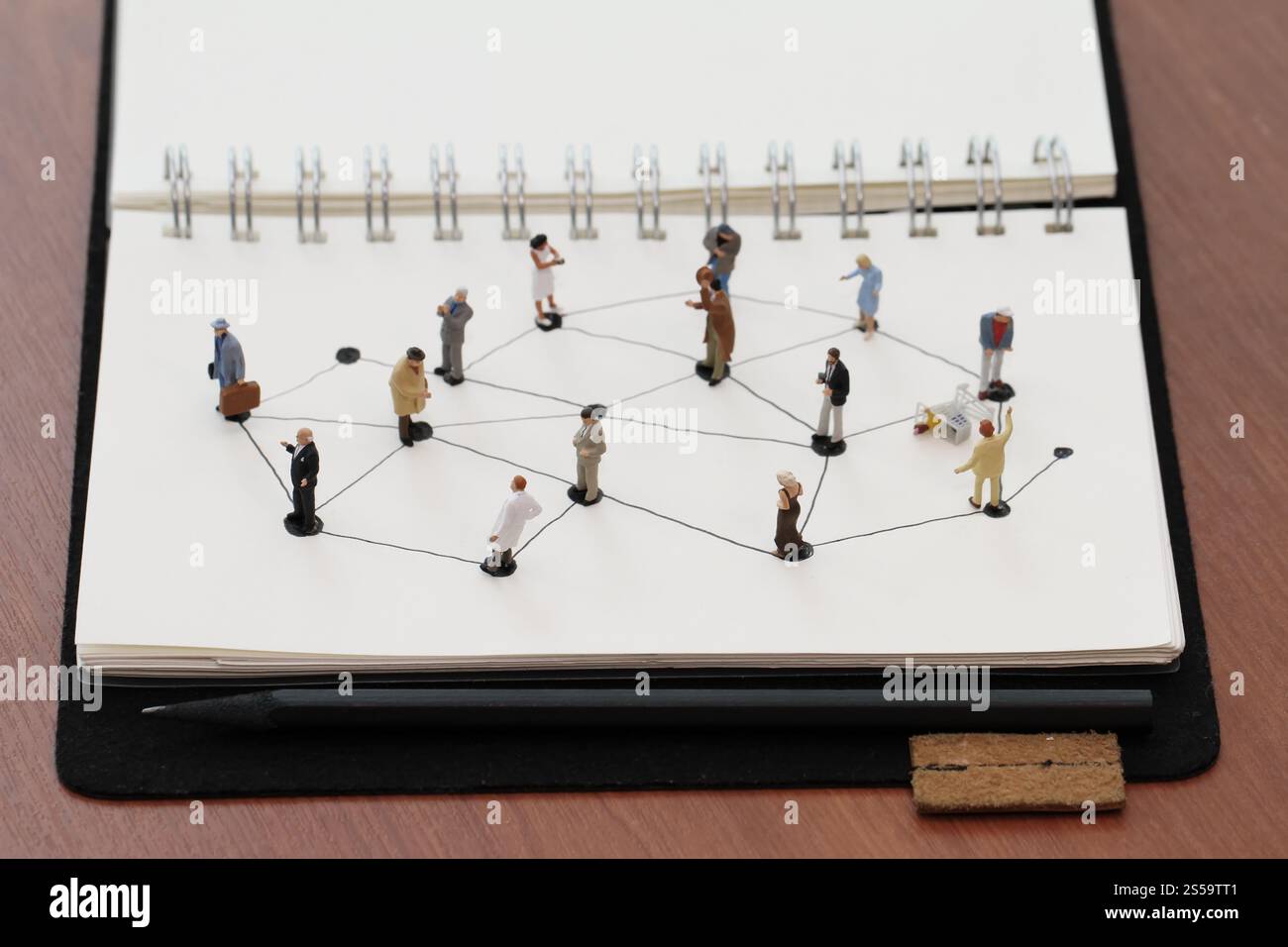 primo piano di persone in miniatura con un diagramma di social network su un notebook aperto su una scrivania in legno mentre i social media si avvicinano Foto Stock