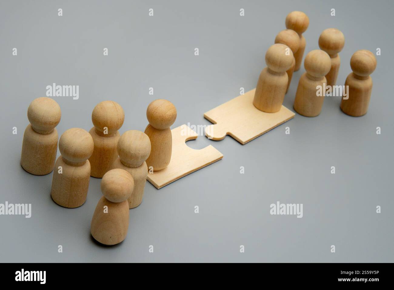 Due gruppi di figure di legno si trovano sui lati opposti di un ponte di pezzi di puzzle. Fusioni e acquisizioni, integrazione aziendale e combinazione delle forze Foto Stock