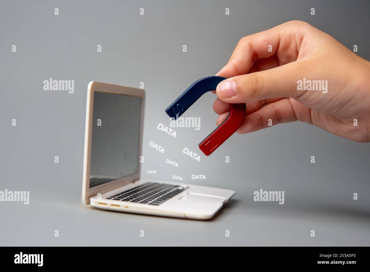 Una mano che tiene un magnete vicino allo schermo di un laptop con la parola "DATI". Violazioni dei dati e vulnerabilità del concetto di informazioni digitali. Foto Stock