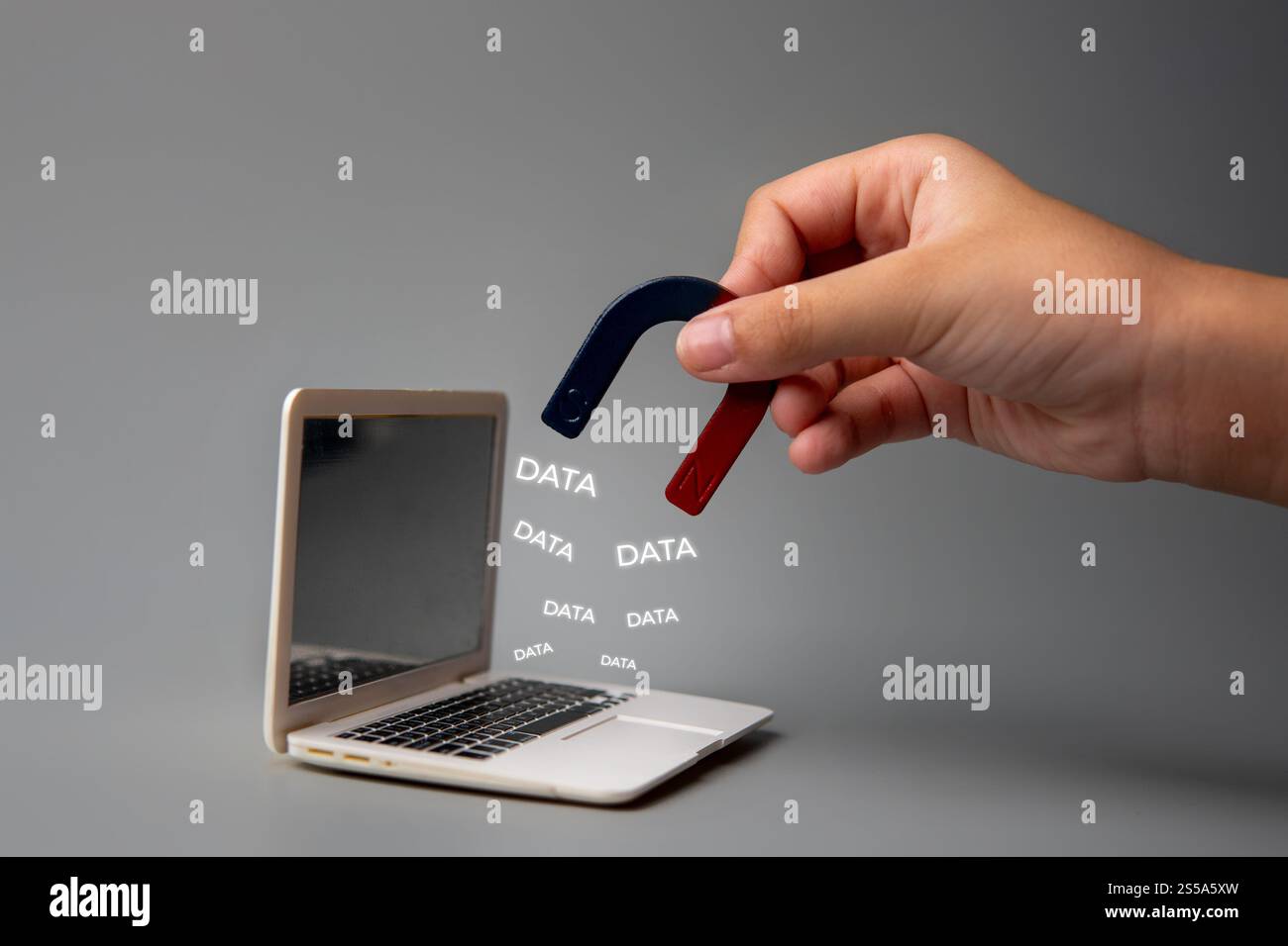 Una mano che tiene un magnete vicino allo schermo di un laptop con la parola "DATI". Violazioni dei dati e vulnerabilità del concetto di informazioni digitali. Foto Stock