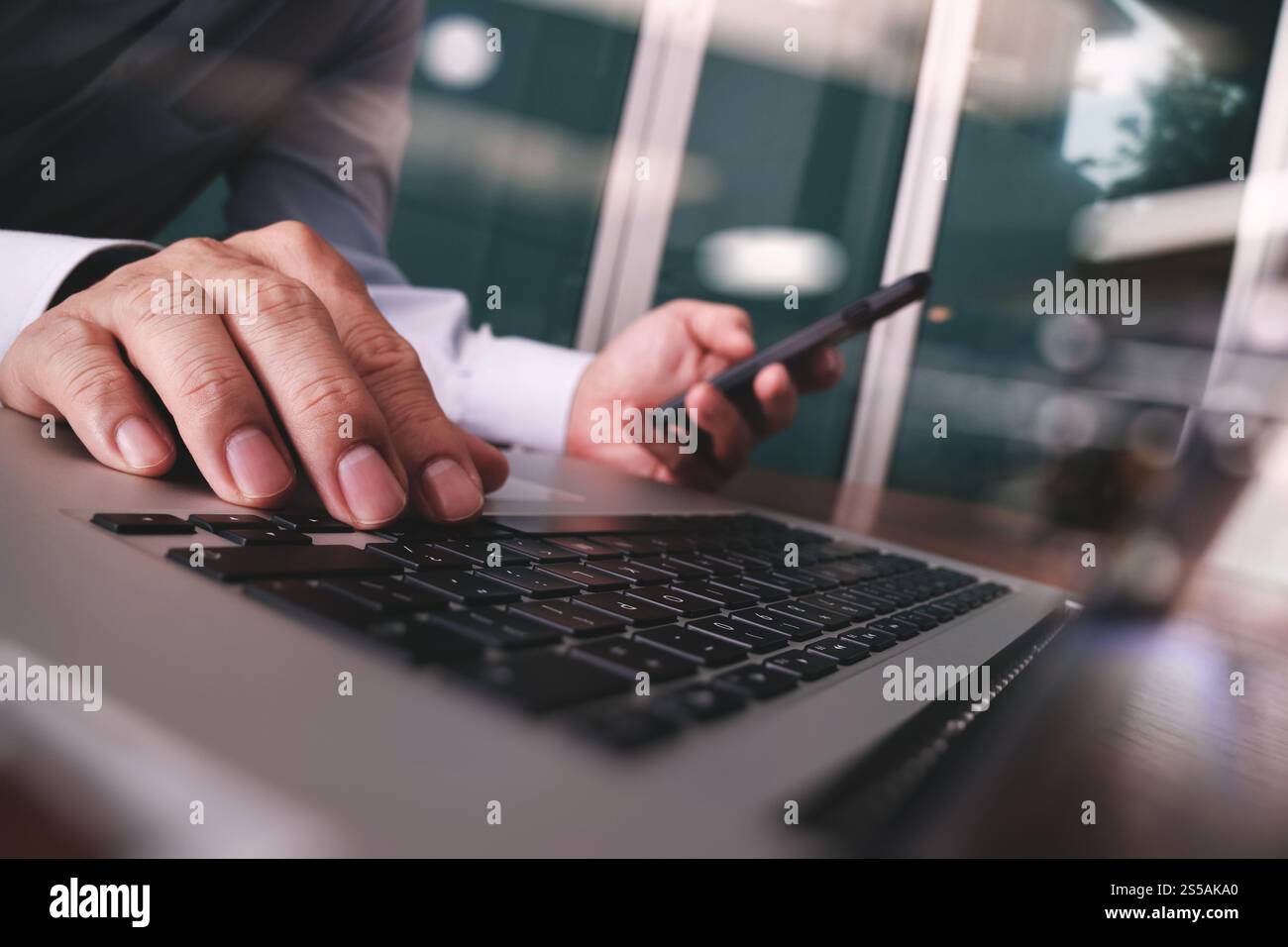 Close up di business man mano lavorando sul computer portatile con smart phone sulla scrivania di legno come concetto Foto Stock