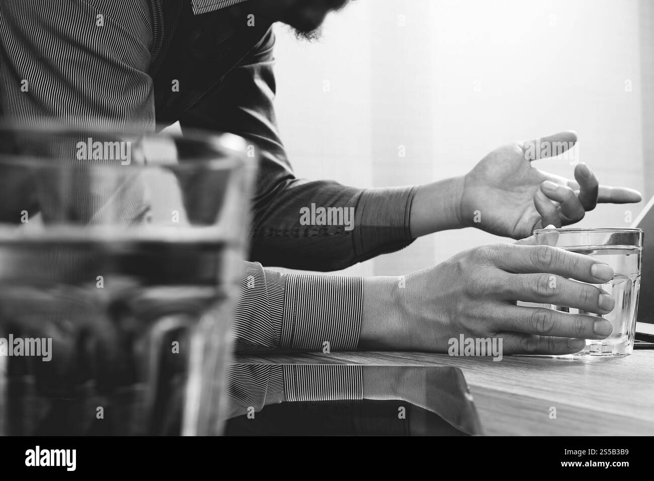 Sito web designer mano che tiene un bicchiere di acqua lavorando tavoletta digitale e computer laptop sulla scrivania in legno,bianco nero Foto Stock
