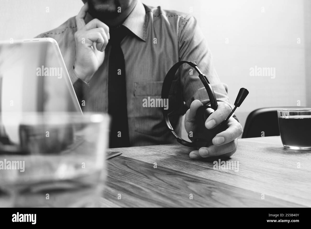 Business man utilizzando cuffie VOIP con tavoletta digitale computer docking tastiera intelligente, il concetto di comunicazione, il supporto it,sulla scrivania di legno,bianco nero Foto Stock