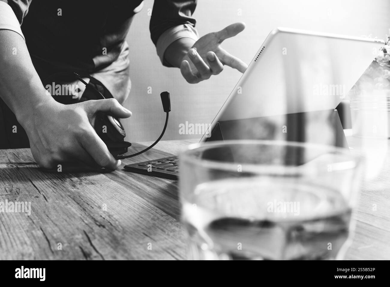 Business man utilizzando cuffie VOIP con tavoletta digitale computer docking tastiera intelligente, il concetto di comunicazione, il supporto it,sulla scrivania di legno,bianco nero Foto Stock