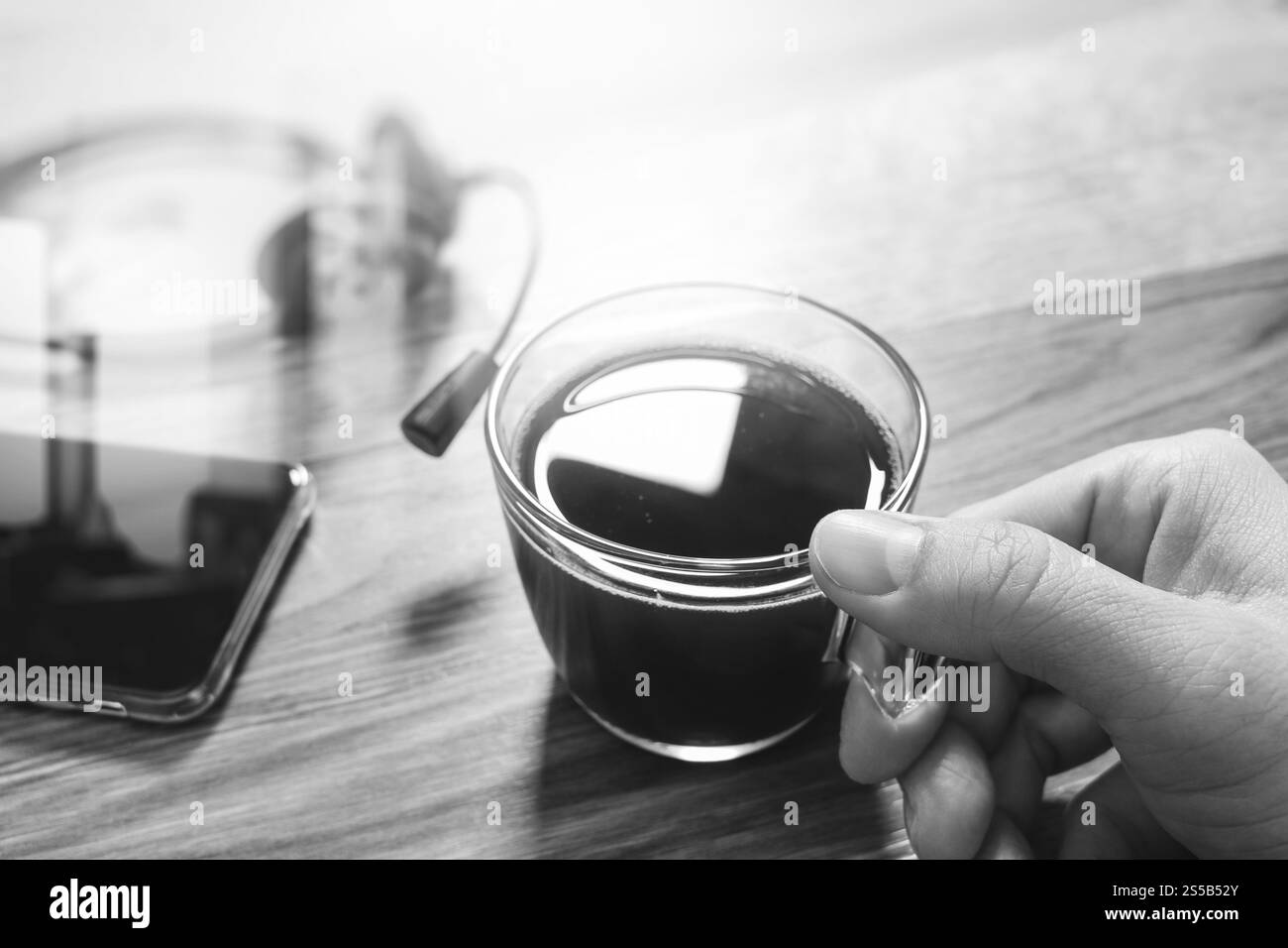 Mano azienda tazza di caffè o tè e cuffie voip,smart phone sul tavolo di legno,l'effetto filtro,bianco nero Foto Stock
