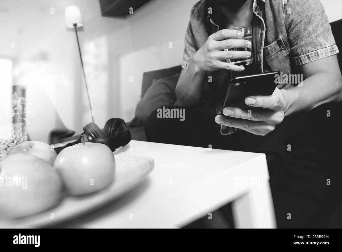 uomo di design a mano che utilizza pagamenti mobili shopping online, omni channel, acqua potabile, seduto sul divano nel soggiorno, mele verdi nel vassoio di legno, nero Foto Stock