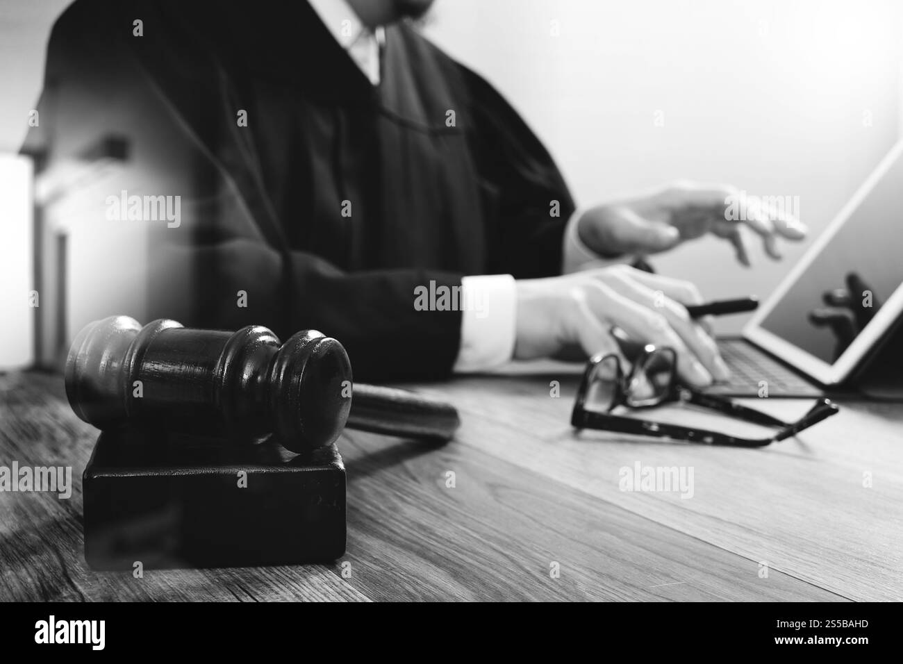 concetto di giustizia e diritto. Giudice maschile in un'aula di tribunale con il martelletto, che lavora con tablet digitale, computer docking tastiera su tavolo di legno, occhiali, nero Foto Stock