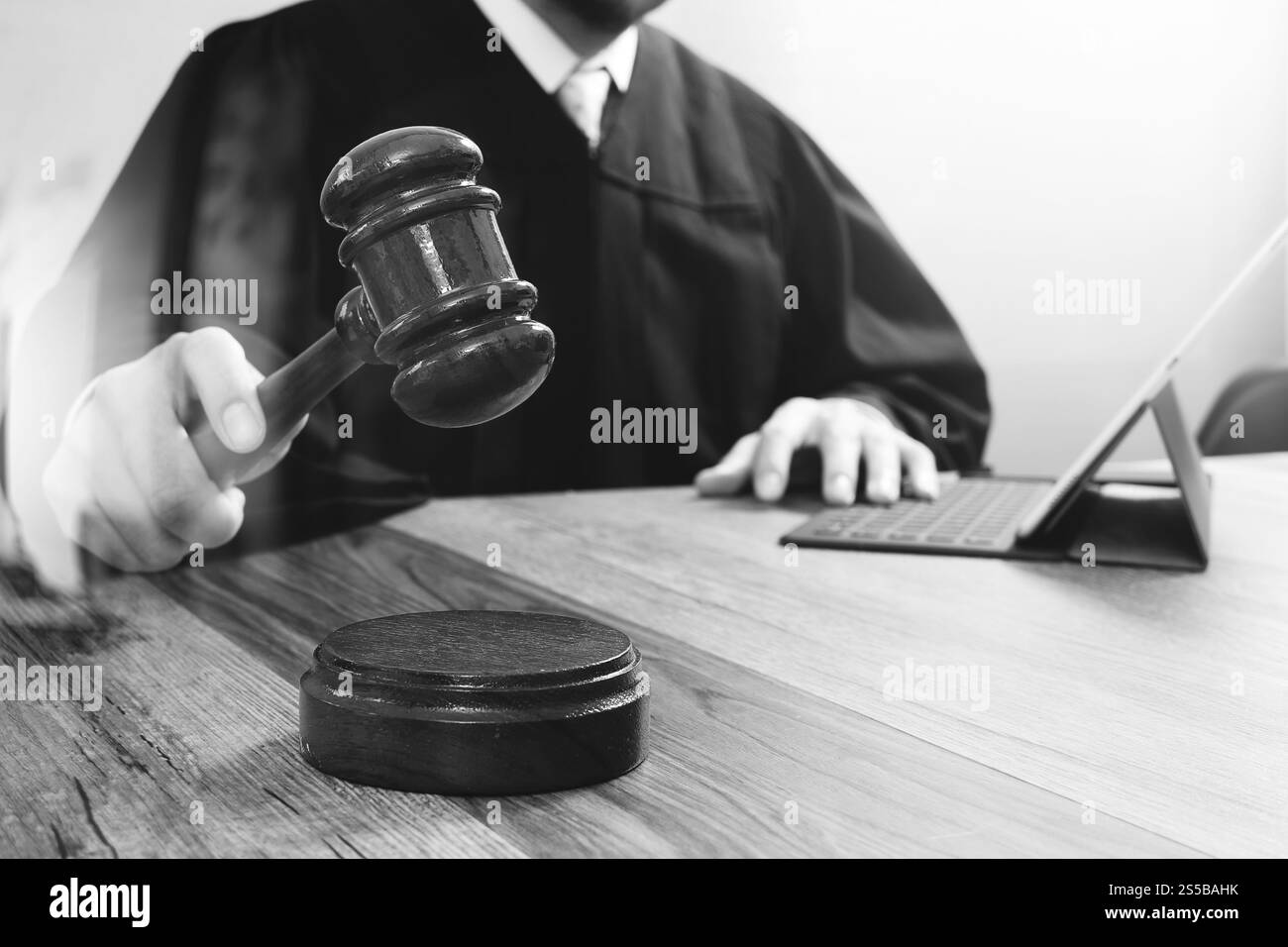 concetto di giustizia e diritto. Giudice maschile in un'aula di tribunale che colpisce il martelletto, lavora con tablet digitale computer docking tastiera su tavolo di legno, nero e. Foto Stock