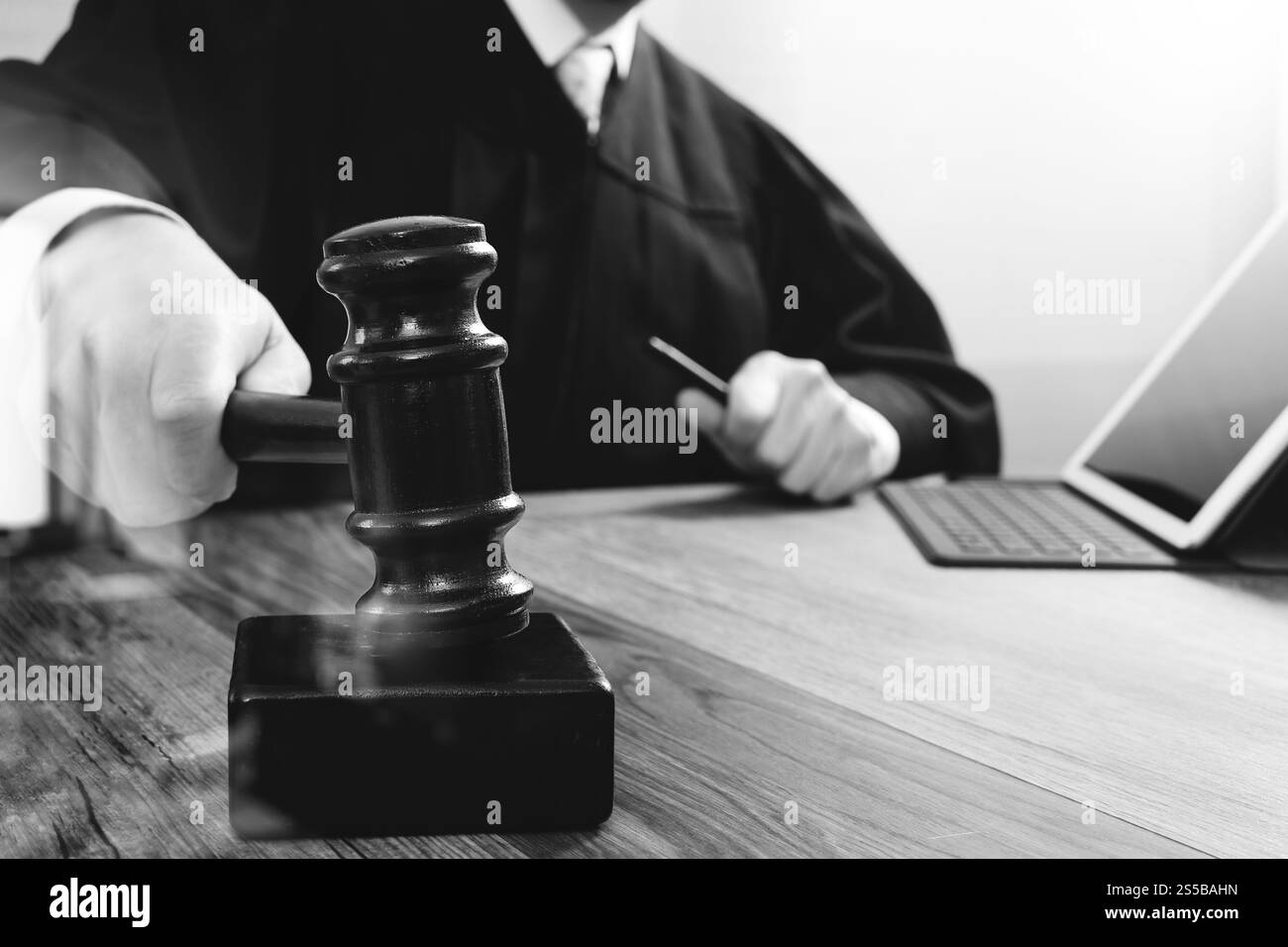 concetto di giustizia e diritto. Giudice maschile in un'aula di tribunale che colpisce il martelletto, lavora con tablet digitale computer docking tastiera su tavolo di legno, nero e. Foto Stock