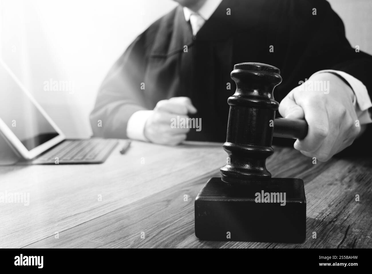 concetto di giustizia e diritto. Giudice maschile in un'aula di tribunale che colpisce il martelletto, lavora con tablet digitale computer docking tastiera su tavolo di legno, nero e. Foto Stock