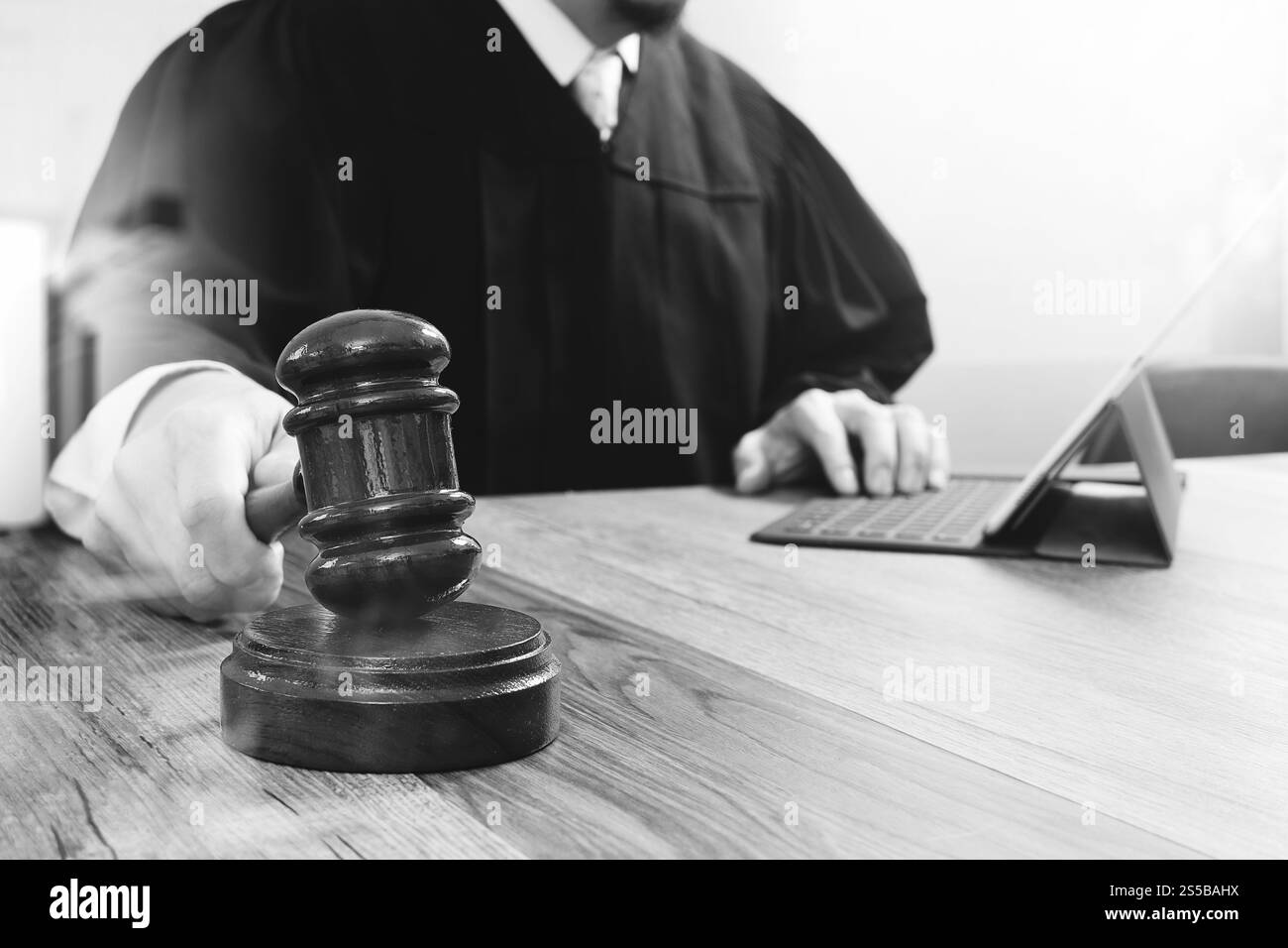 concetto di giustizia e diritto. Giudice maschile in un'aula di tribunale che colpisce il martelletto, lavora con tablet digitale computer docking tastiera su tavolo di legno, nero e. Foto Stock