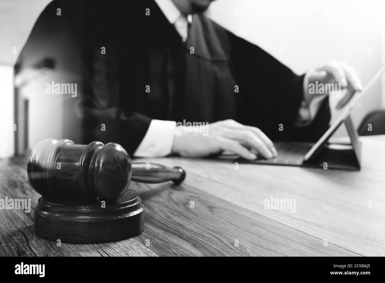 La giustizia e la nozione di diritto.Giudice maschi nelle aule di un tribunale con il martello,lavora con tavoletta digitale computer tastiera docking sulla tavola di legno,in bianco e nero Foto Stock
