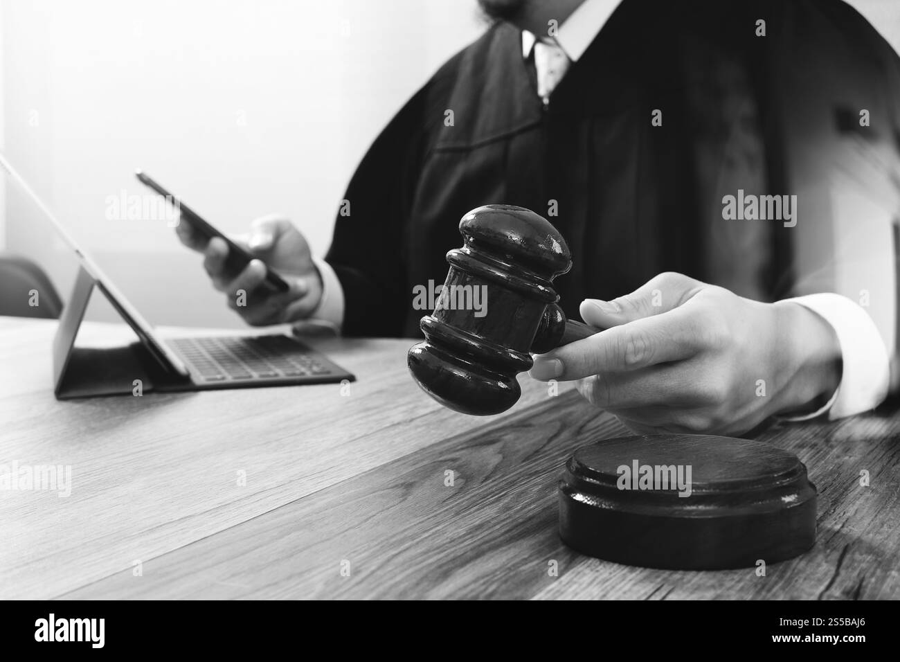 concetto di giustizia e diritto. Giudice maschile in un'aula con il martelletto, che lavora con smartphone, tablet digitale, tastiera docking su legno Foto Stock