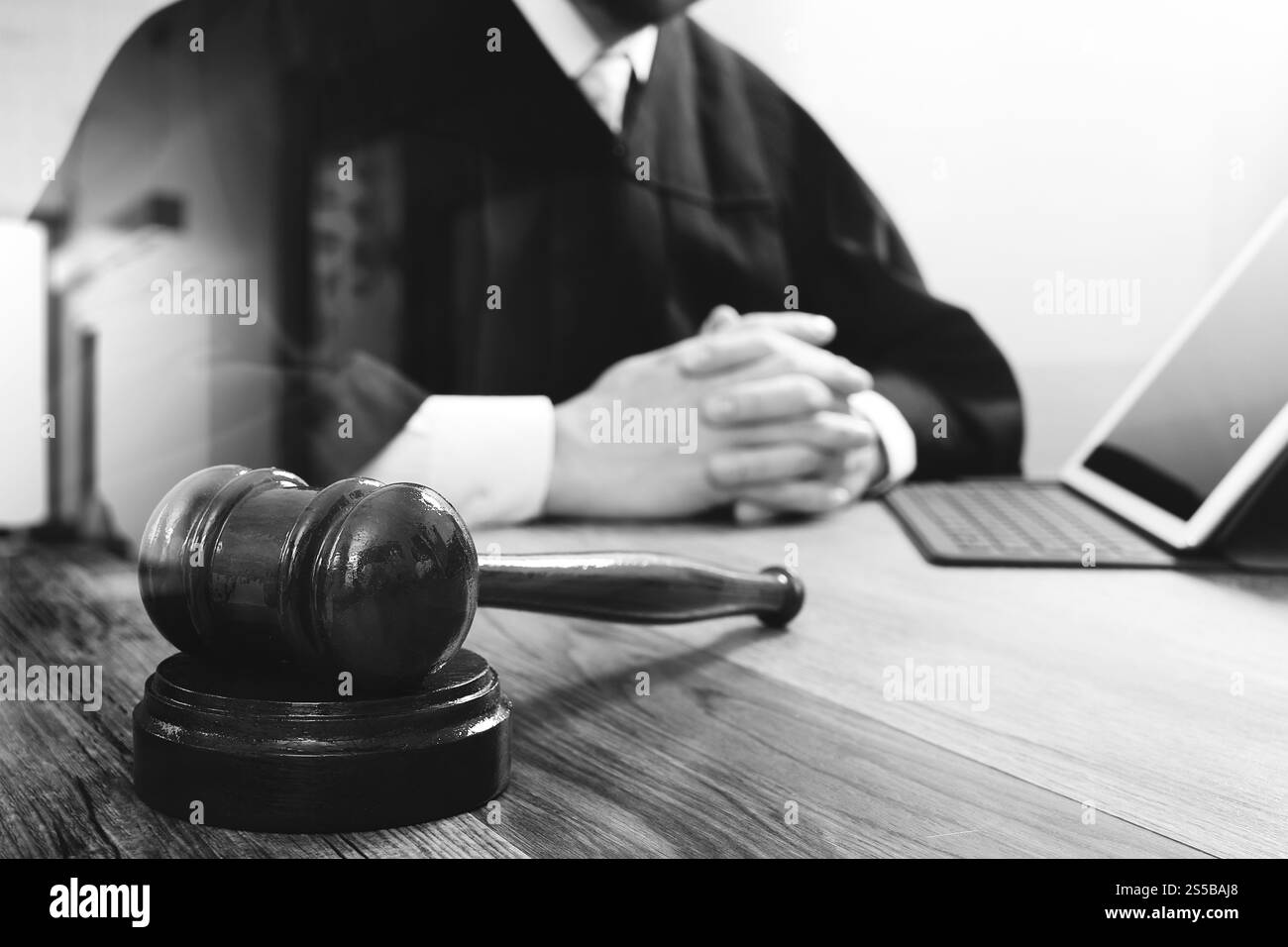 concetto di giustizia e diritto. Giudice maschile in un'aula di tribunale con il martelletto, che lavora con tablet digitale, computer docking tastiera su tavolo di legno, occhiali, nero Foto Stock