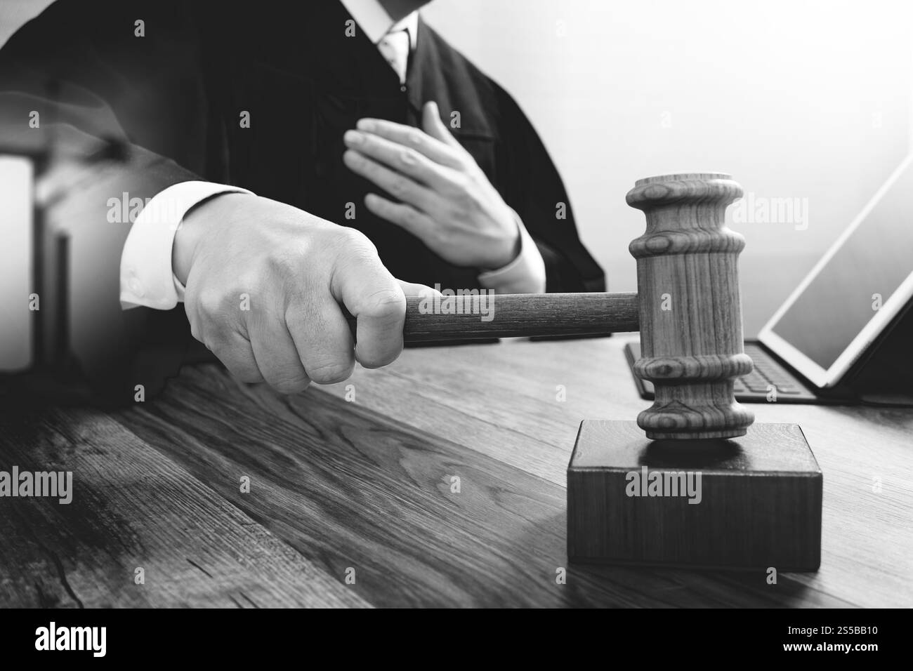 concetto di giustizia e diritto. Giudice maschile in un'aula di tribunale che colpisce il martelletto, lavora con tablet digitale computer docking tastiera su tavolo di legno, nero e. Foto Stock
