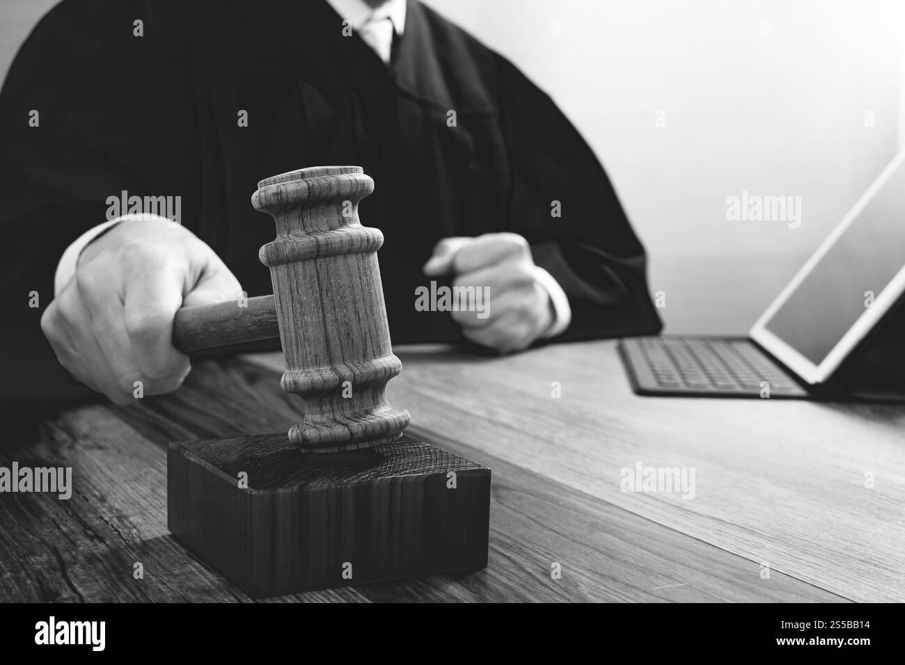 concetto di giustizia e diritto. Giudice maschile in un'aula di tribunale che colpisce il martelletto, lavora con tablet digitale computer docking tastiera su tavolo di legno, nero e. Foto Stock