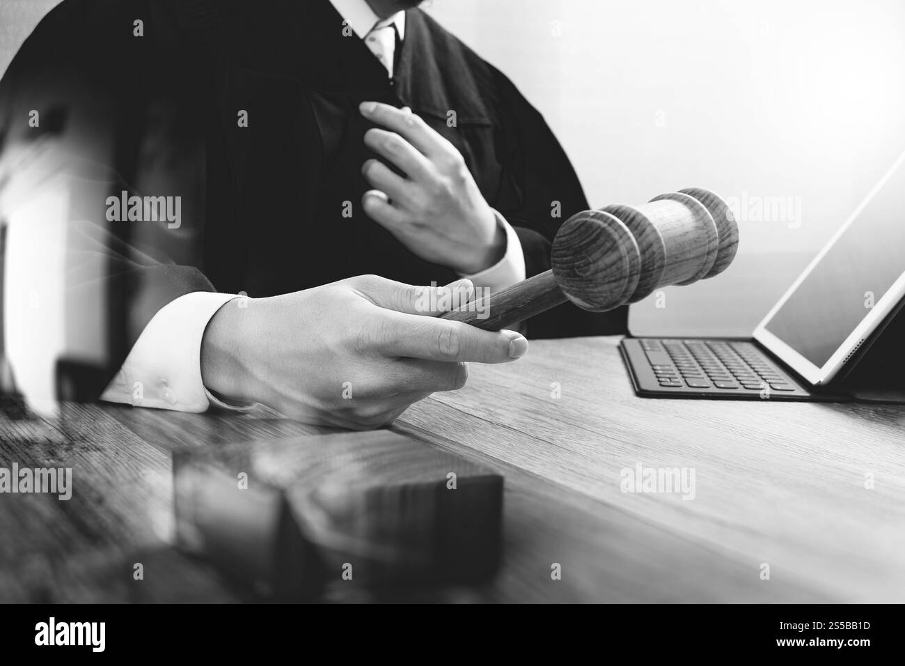La giustizia e la nozione di diritto.Giudice maschi nelle aule di un tribunale con il martello,lavora con tavoletta digitale computer tastiera docking sulla tavola di legno,in bianco e nero Foto Stock