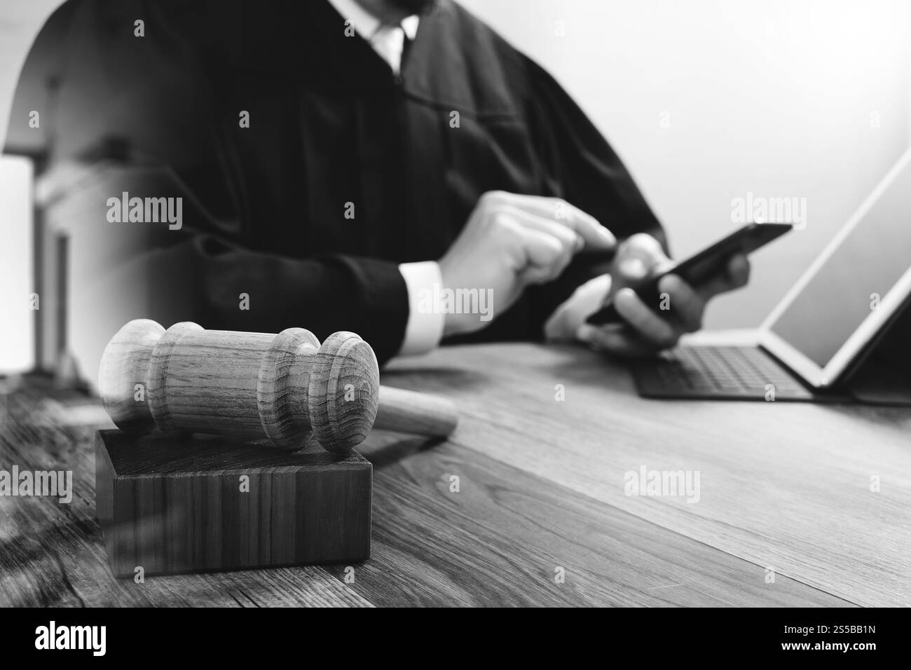 concetto di giustizia e diritto. Giudice maschile in un'aula con il martelletto, che lavora con lo smartphone, tablet digitale, tastiera docking su legno Foto Stock