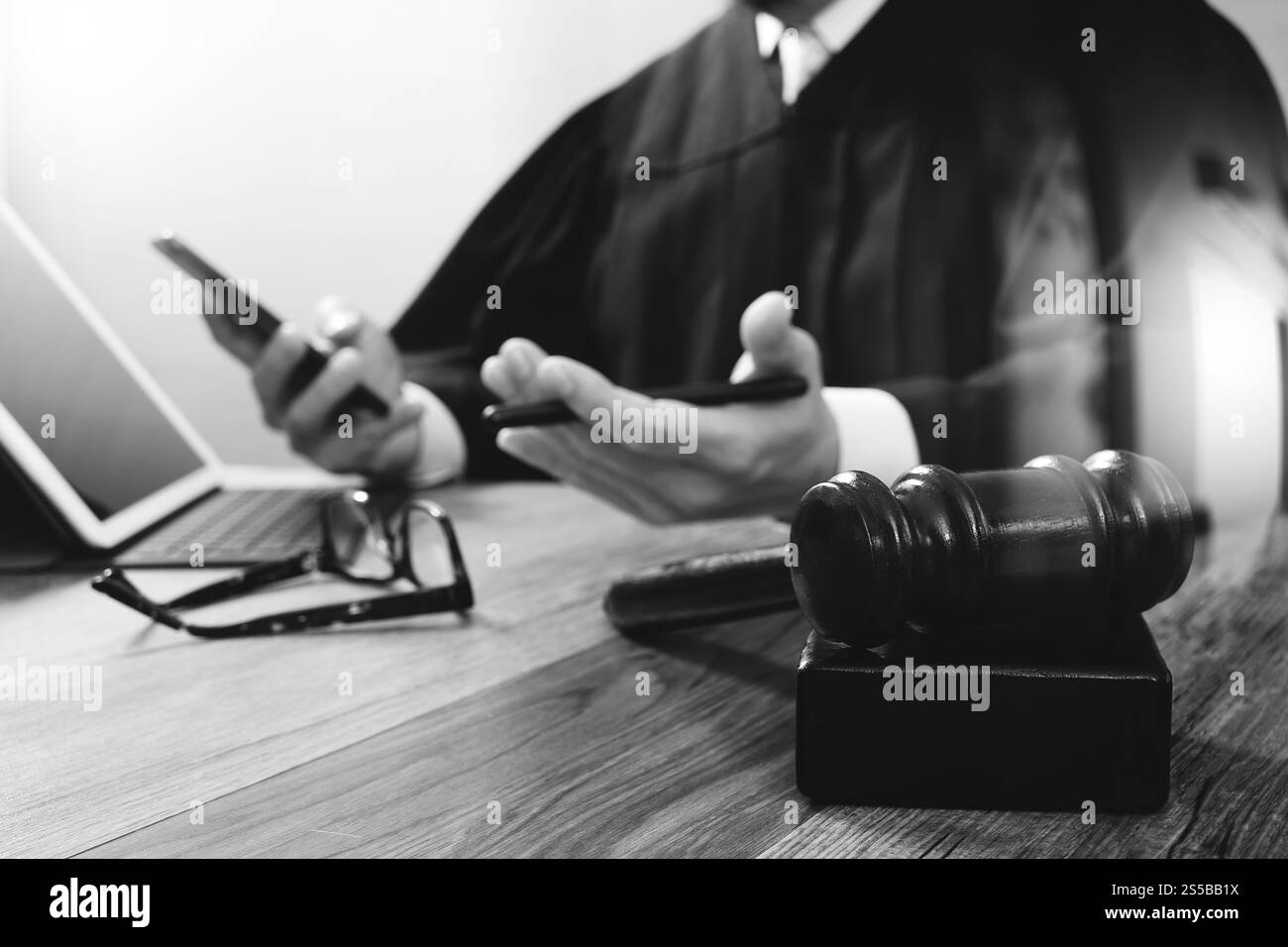 concetto di giustizia e diritto. Giudice maschile in un'aula con il martelletto, che lavora con lo smartphone, tablet digitale, tastiera docking su legno Foto Stock