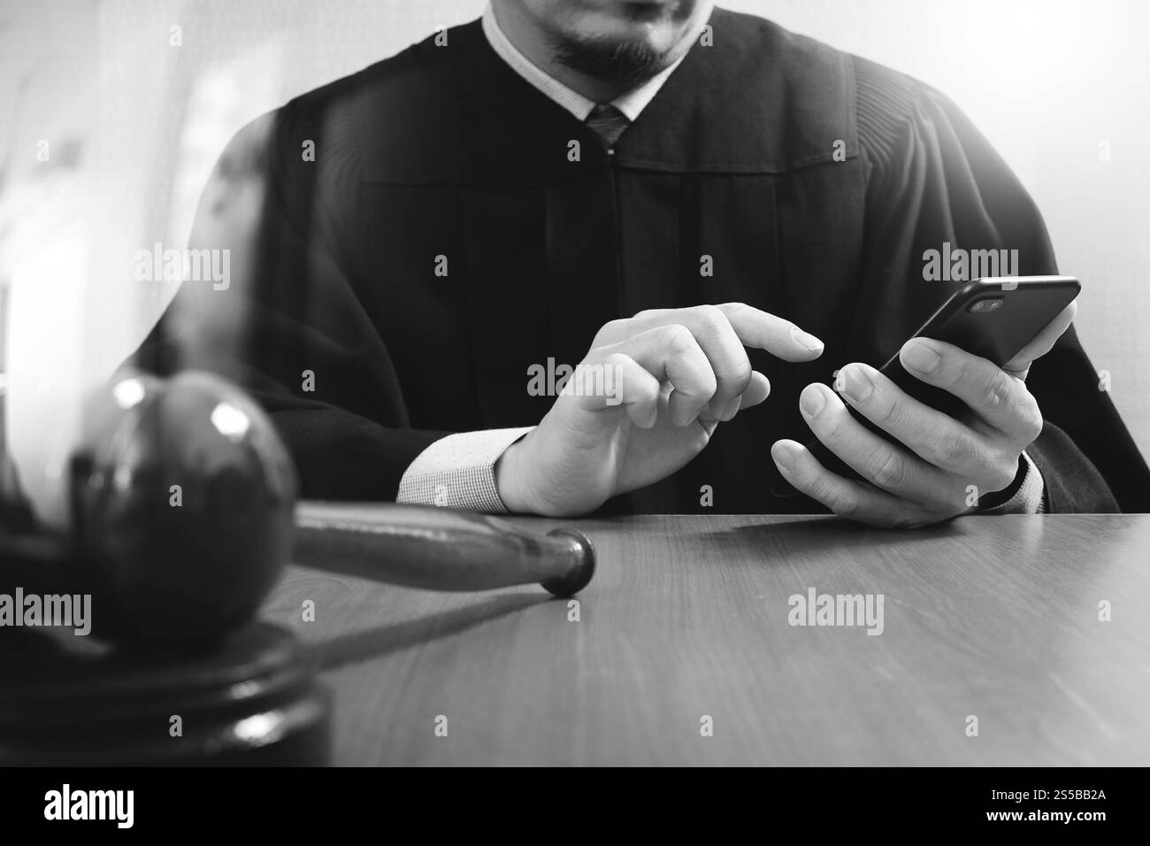 concetto di giustizia e diritto. Giudice maschile in un'aula di tribunale con il martelletto, che lavora con il computer dello smartphone su un tavolo di legno, bianco e nero Foto Stock