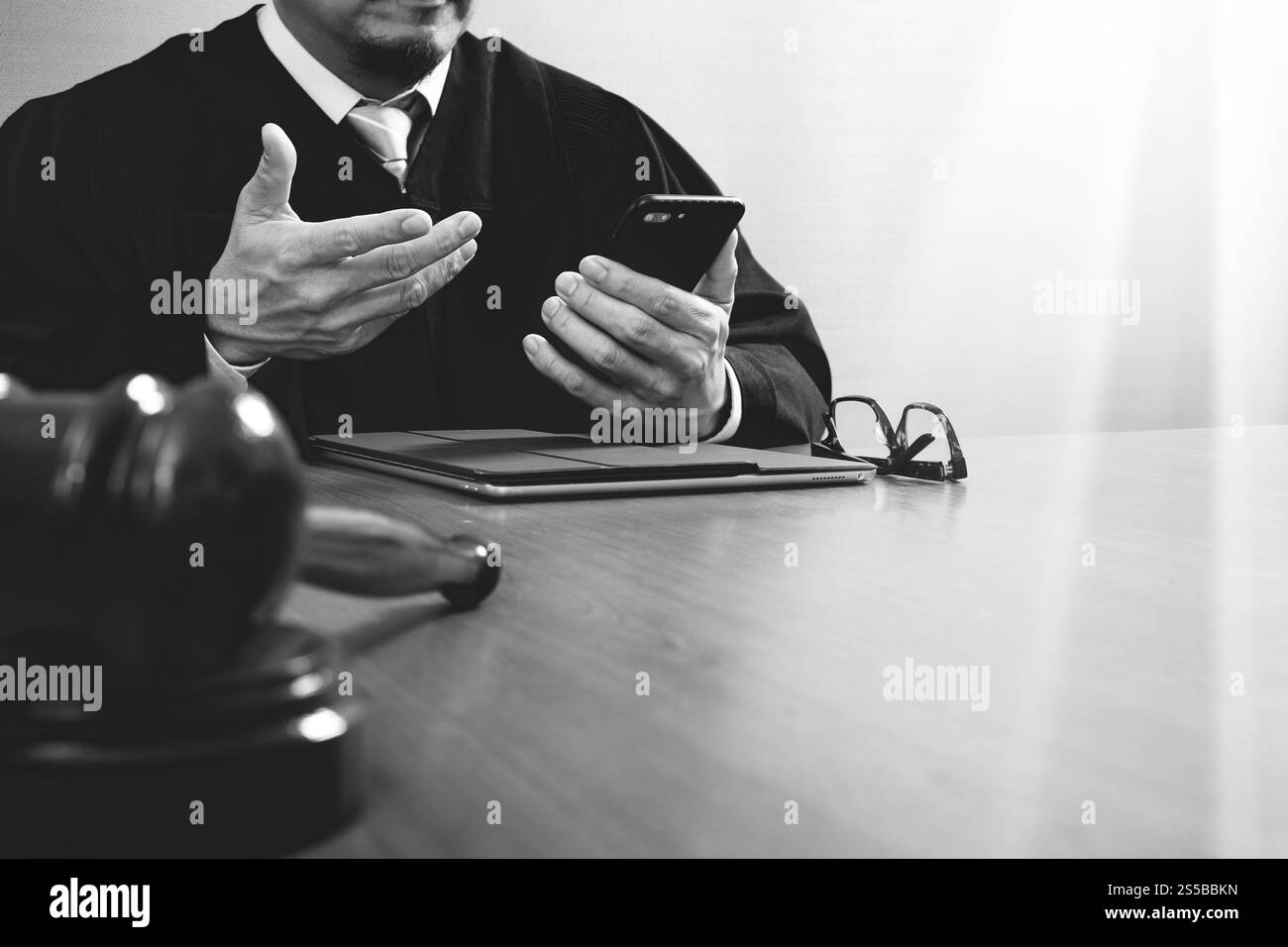 concetto di giustizia e diritto. Giudice maschile in un'aula con il martelletto, che lavora con lo smartphone, tablet digitale, tastiera docking su legno Foto Stock