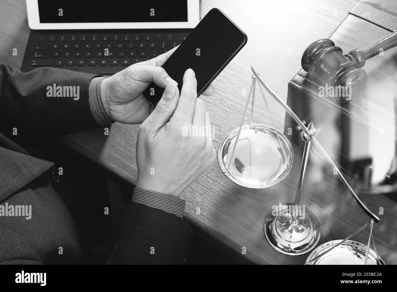 concetto di giustizia e diritto. Avvocato maschile in ufficio con il martelletto, lavorare con smartphone, tablet digitale computer docking tastiera, bilancia in ottone, su legno Foto Stock