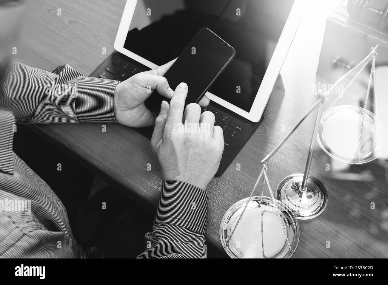 concetto di giustizia e diritto. Avvocato maschile in ufficio con il martelletto, lavorare con smartphone, tablet digitale computer docking tastiera, bilancia in ottone, su legno Foto Stock