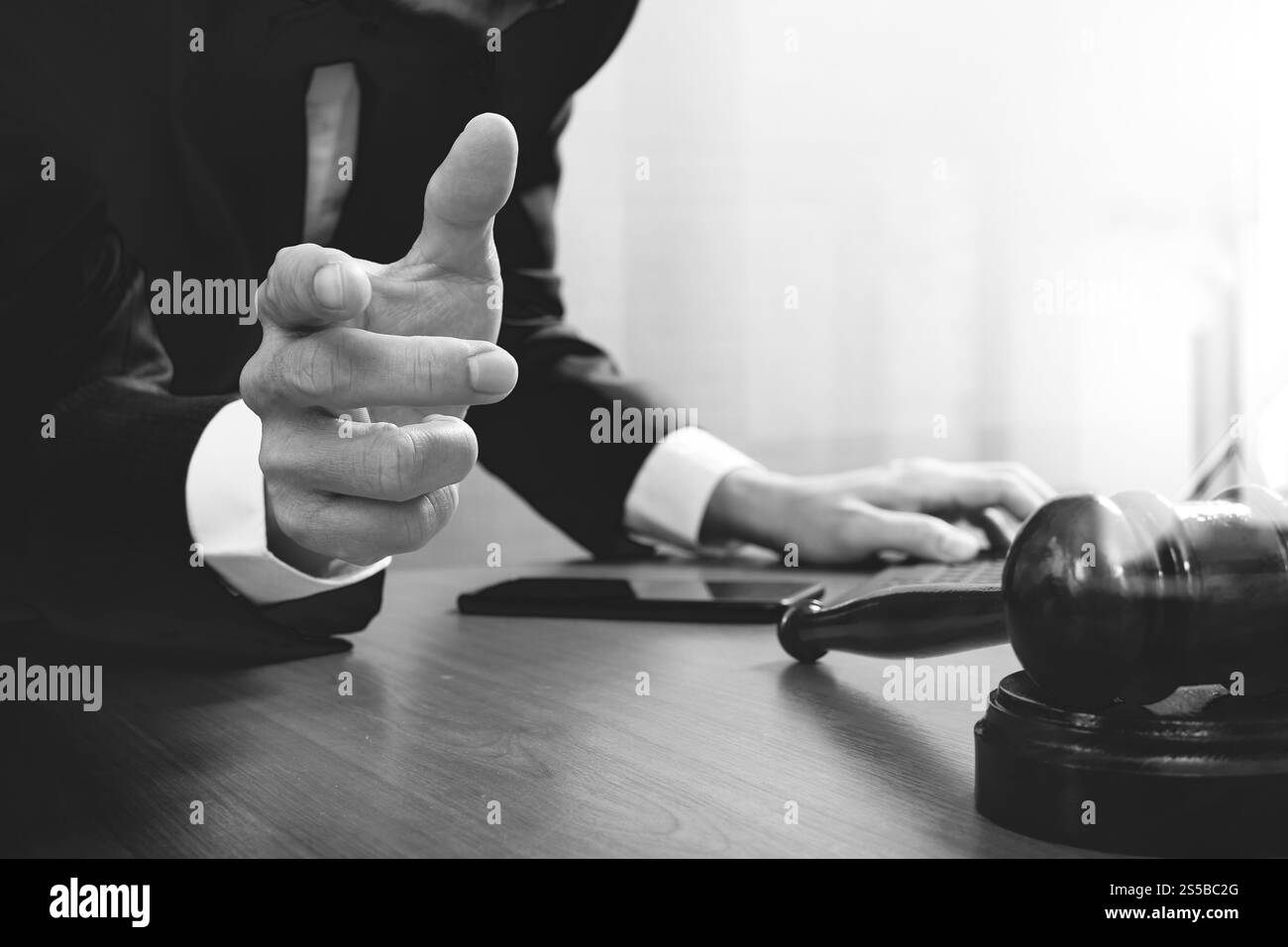 concetto di giustizia e diritto. Avvocato maschile in ufficio con il martelletto, lavorare con smartphone, tablet digitale computer docking tastiera, bilancia in ottone, su legno Foto Stock