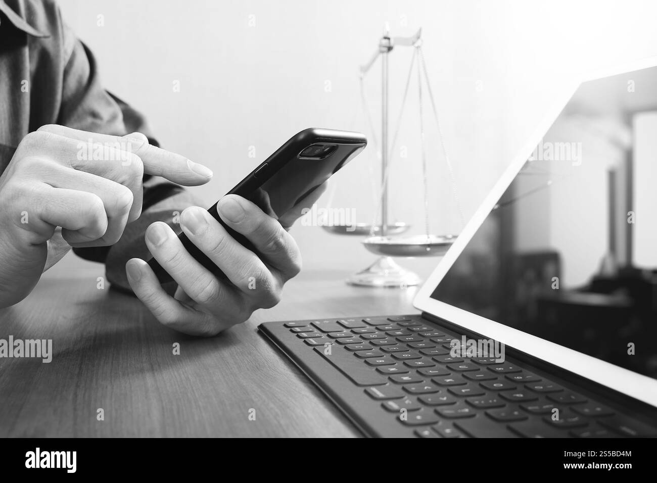 concetto di giustizia e diritto. Avvocato maschile in ufficio con bilancia in ottone, lavoro a mano con smartphone e tablet digitale su legno Foto Stock