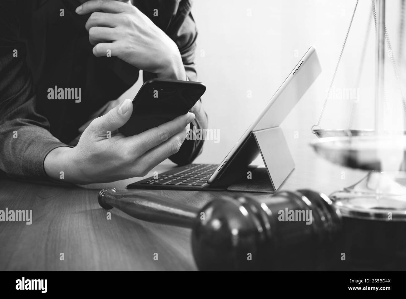 La giustizia e la nozione di diritto.avvocato maschio in ufficio con il martello,lavora con smart phone e digital computer tablet e scala di ottone su tavola di legno,nero Foto Stock