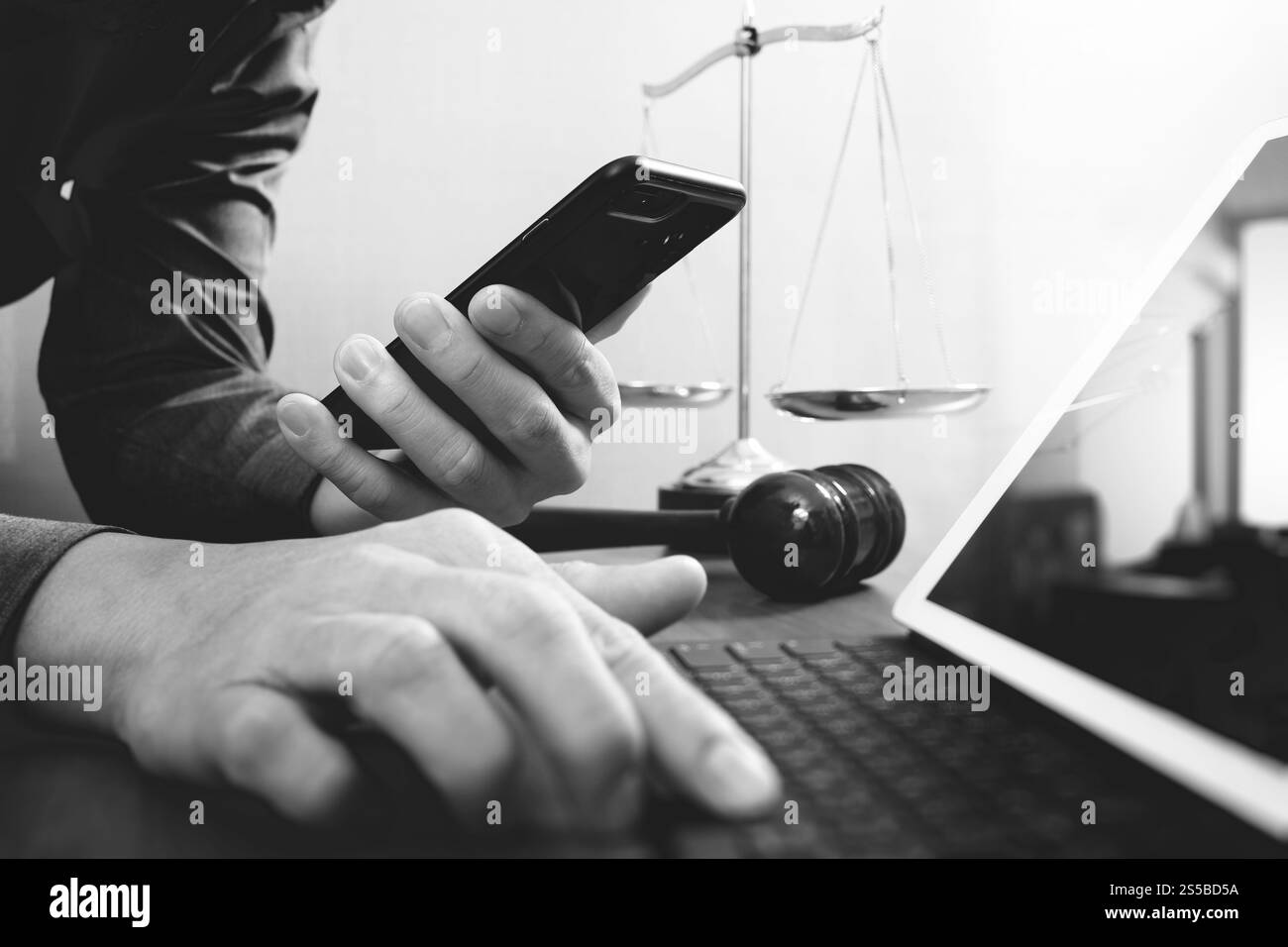 La giustizia e la nozione di diritto.avvocato maschio in ufficio con il martello,lavora con smart phone e digital computer tablet e scala di ottone su tavola di legno,nero Foto Stock