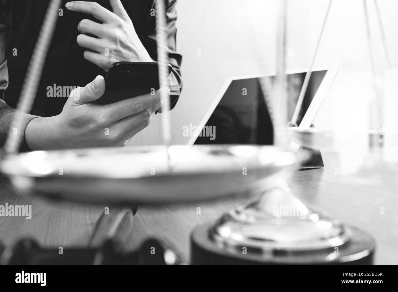 La giustizia e la nozione di diritto.avvocato maschio in ufficio con il martello,lavora con smart phone e digital computer tablet e scala di ottone su tavola di legno,nero Foto Stock