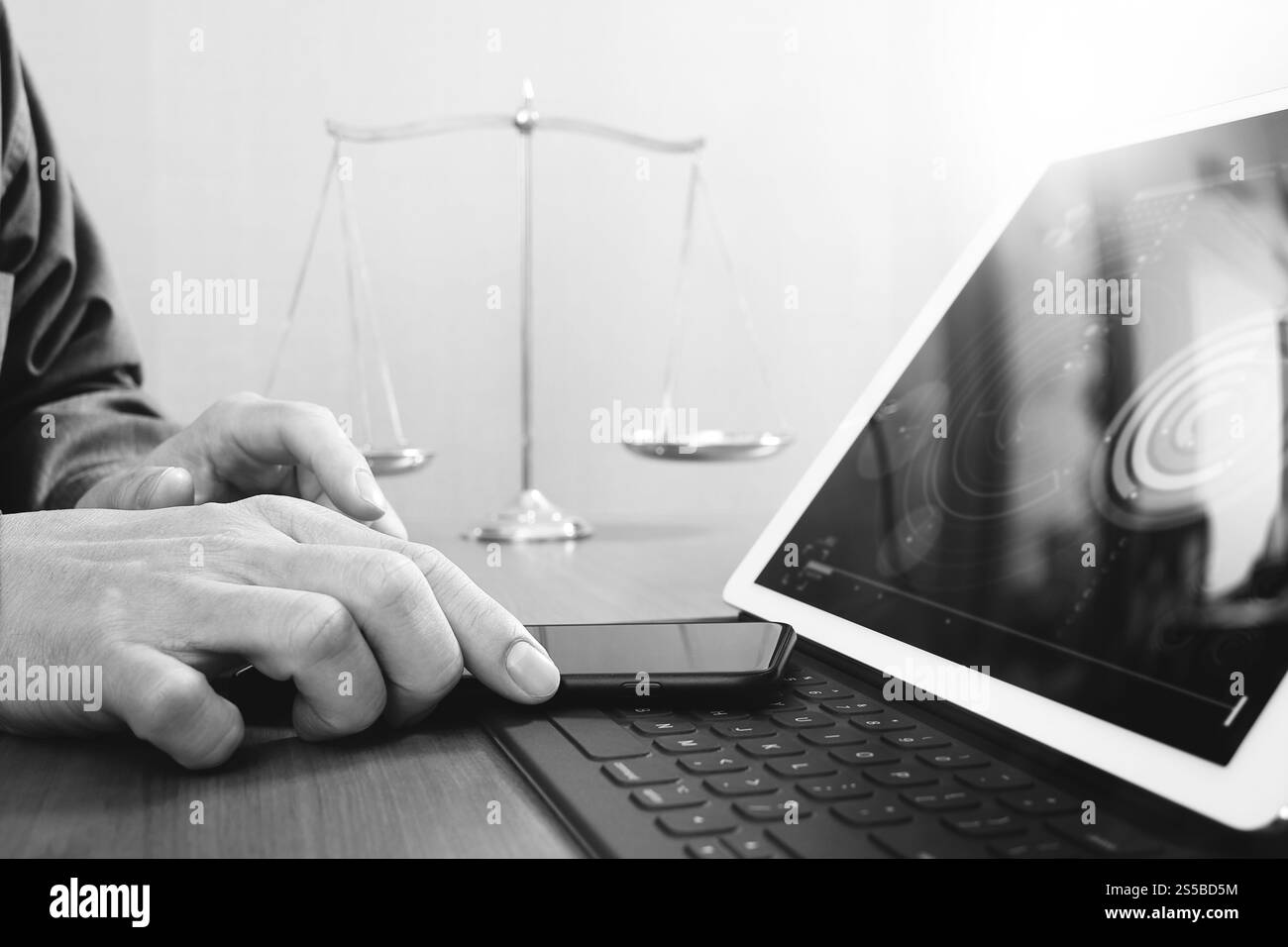 La giustizia e la nozione di diritto.avvocato maschio in ufficio con il martello,lavora con smart phone e digital computer tablet e scala di ottone su tavola di legno,nero Foto Stock