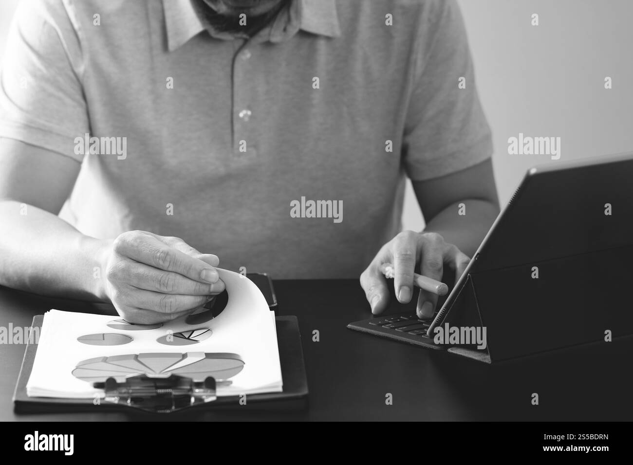 Imprenditore nel t-shirt rosa lavora con digitali computer tablet e apertura del documento sulla scrivania di legno in un ufficio moderno,in bianco e nero Foto Stock