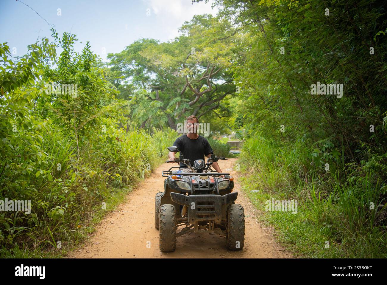 Vista posteriore di un uomo sorridente che guida un ATV attraverso la giungla, Coxen Hole, Roatan, Honduras Foto Stock