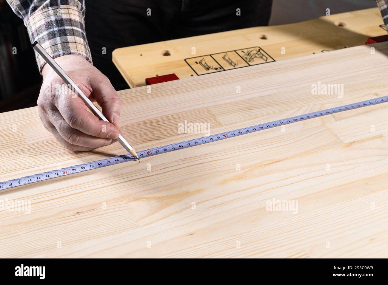 mano di carpentiere con matita misura segni su asse di legno con nastro di misurazione sul banco da lavoro a casa Foto Stock