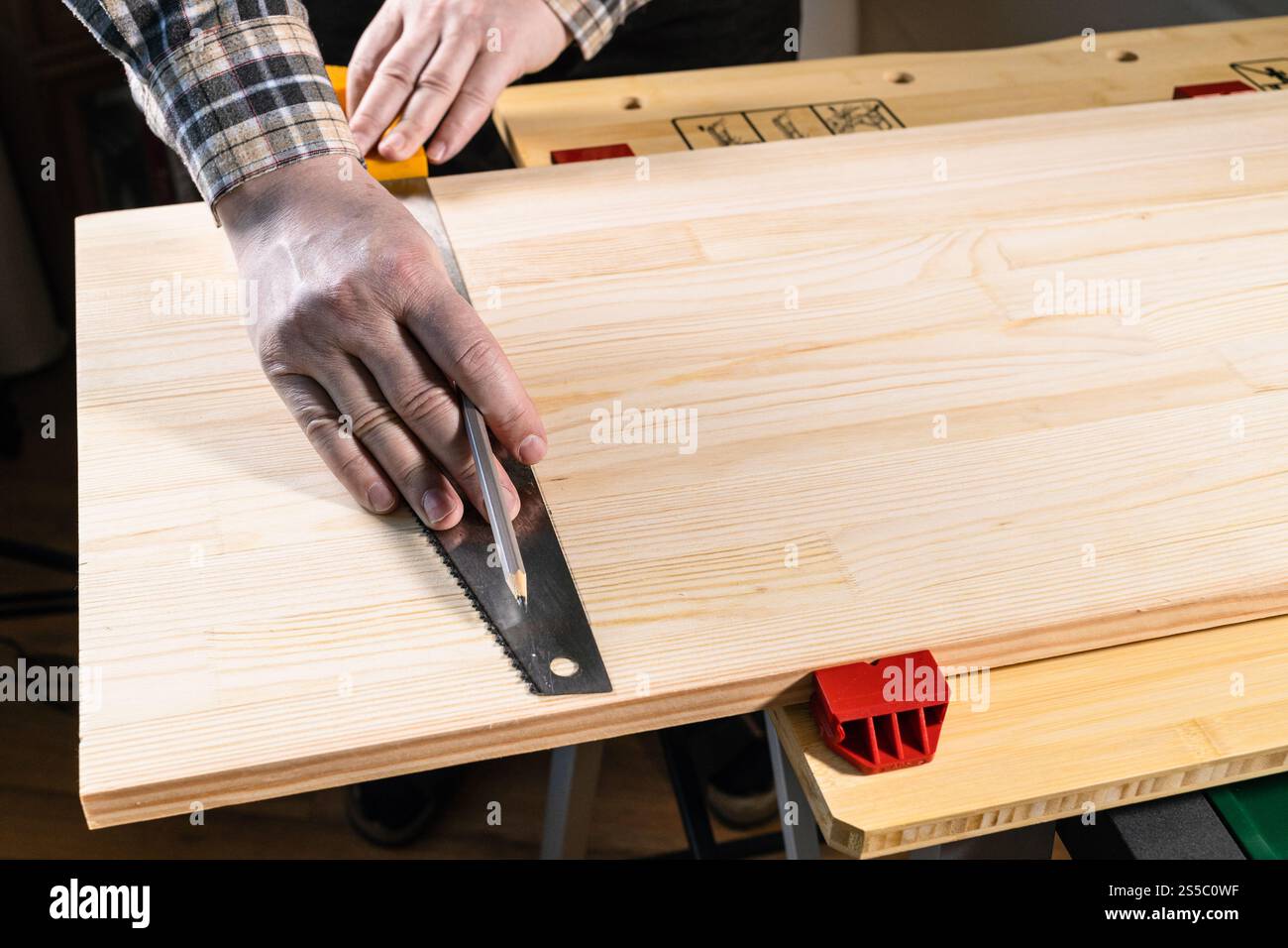il carpentiere segna la linea di taglio sul pannello di legno con lama per sega a mano sul banco da lavoro a casa Foto Stock