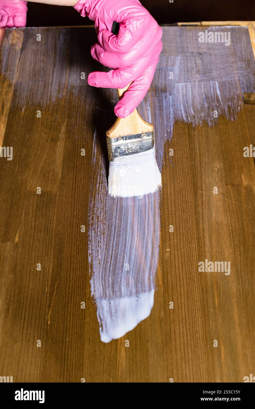 la mano gloved vernicie un asse marrone macchiato della mobilia nel paese Foto Stock