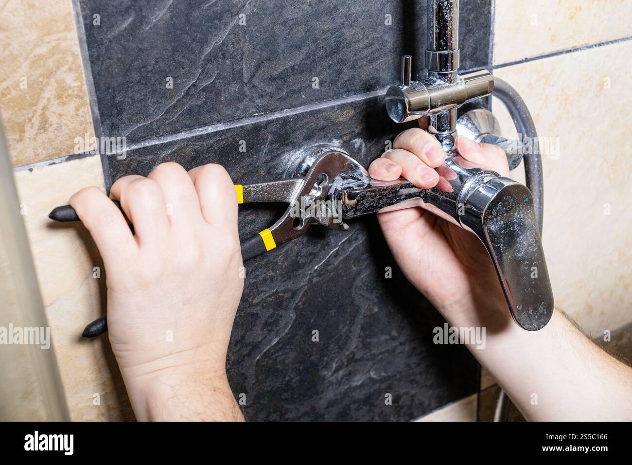 idraulico svitate il rubinetto della doccia sulla parete piastrellata a casa Foto Stock