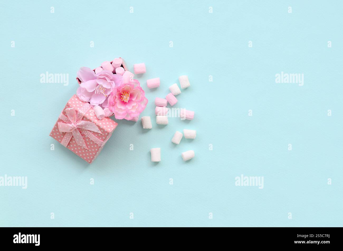 Confezione regalo rosa fiorita cosparsa di marshmallow su sfondo blu. Concetto metaforico lavorazione e coltivazione di fiori. Minimalismo piatto Foto Stock