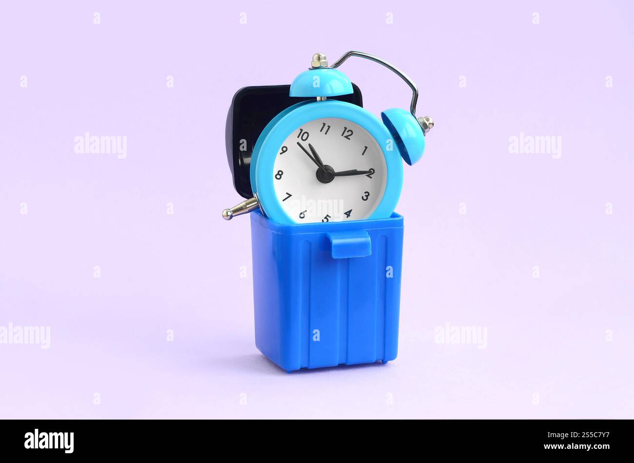 Sprecare tempo. Sveglie blu nel cestino in plastica su sfondo viola. Gestione del tempo sbagliata e sbagliata. Sprecare tempo. Sveglia Foto Stock
