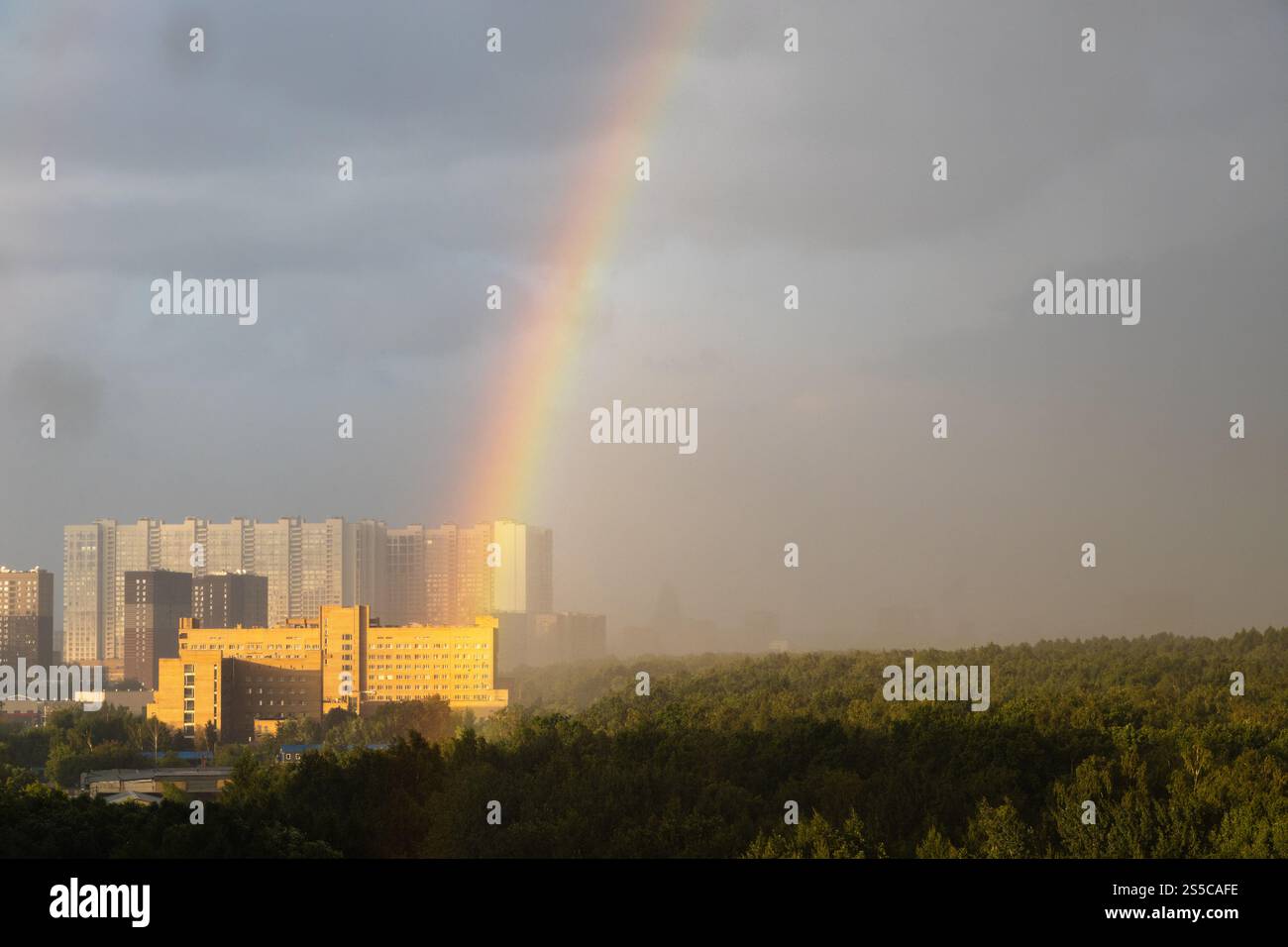 arcobaleno su un alto edificio e parco cittadino sotto la pioggia prima della tempesta di tuoni nella soleggiata giornata estiva Foto Stock