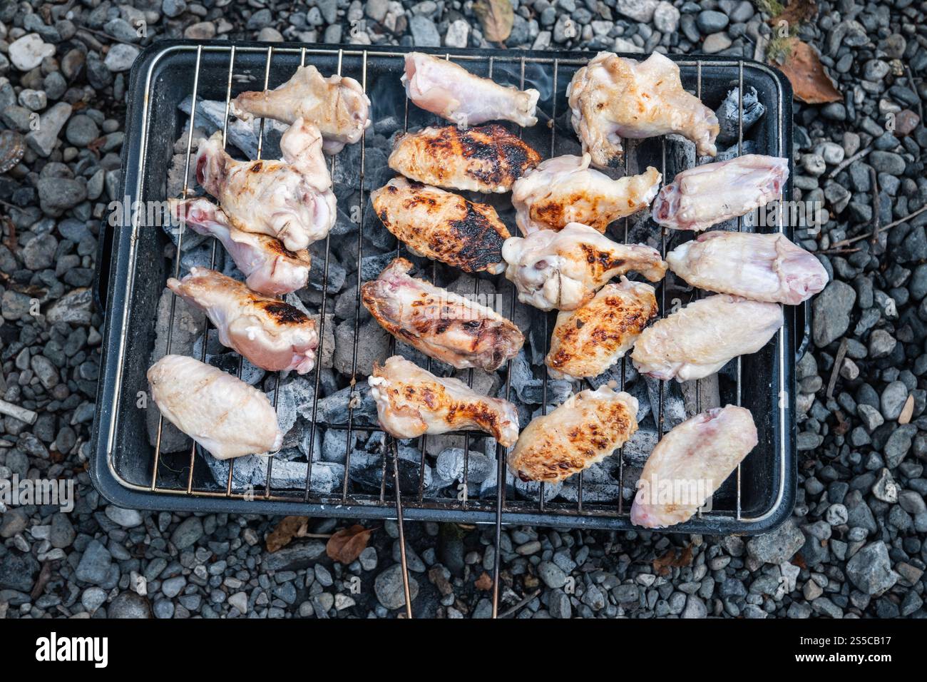 Barbecue all'aperto, Grill Time, varietà di pezzi di pollo crudi, tra cui cosce di pollo e ali di pollo, stuzzicate su una piccola griglia di carbone caldo Foto Stock