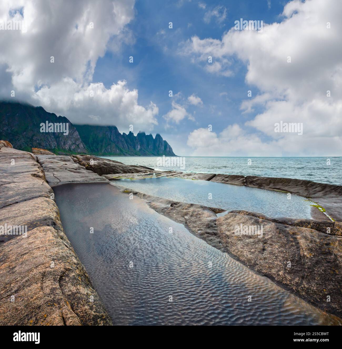 La spiaggia sassosa con bagni di marea a Ersfjord, Senja, Norvegia. Estate giorno polare notte costa. I denti di drago di roccia nel lontano. Foto Stock