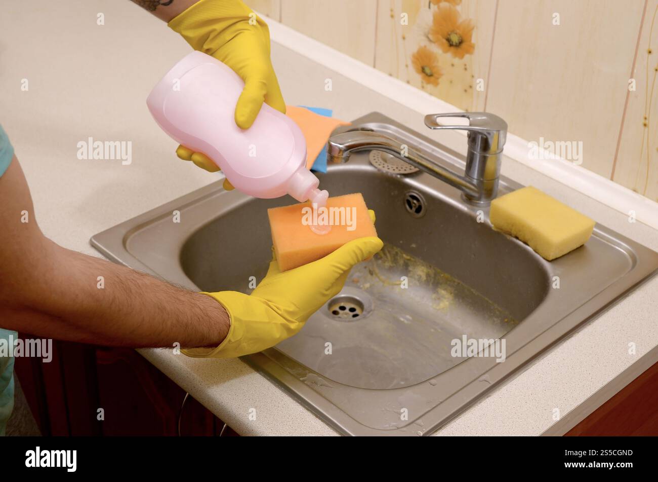 Servizio di pulizia e pulizia della casa. Detergente applicando sapone liquido dal flacone di detergente alla spugna a casa. Uomo in giallo Foto Stock