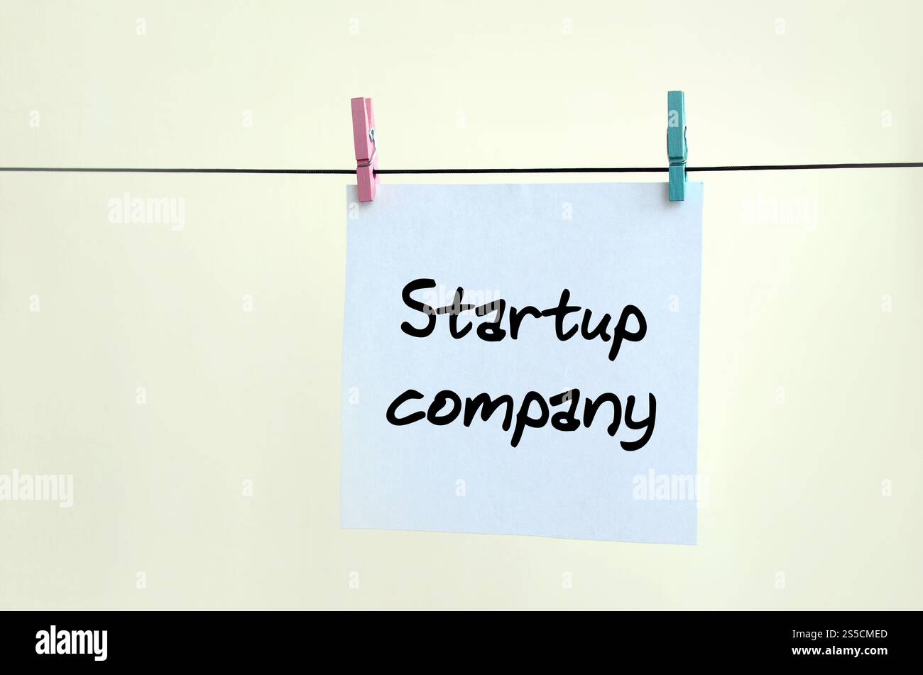 Società di startup. La nota è scritta su un adesivo bianco che appende con una spilla su una corda su uno sfondo di parete beige Foto Stock